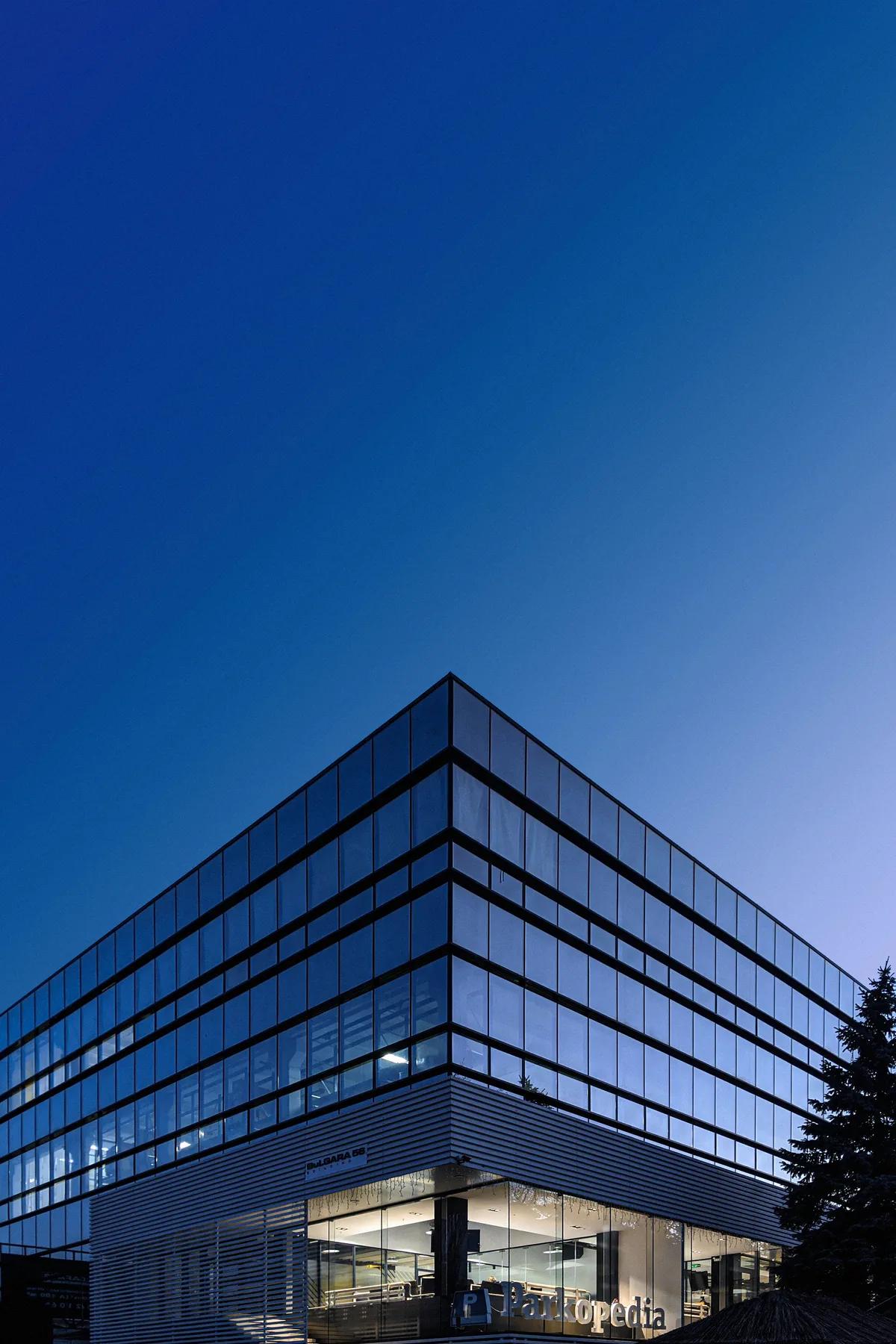 A glass office tower seen from below against a clear sky